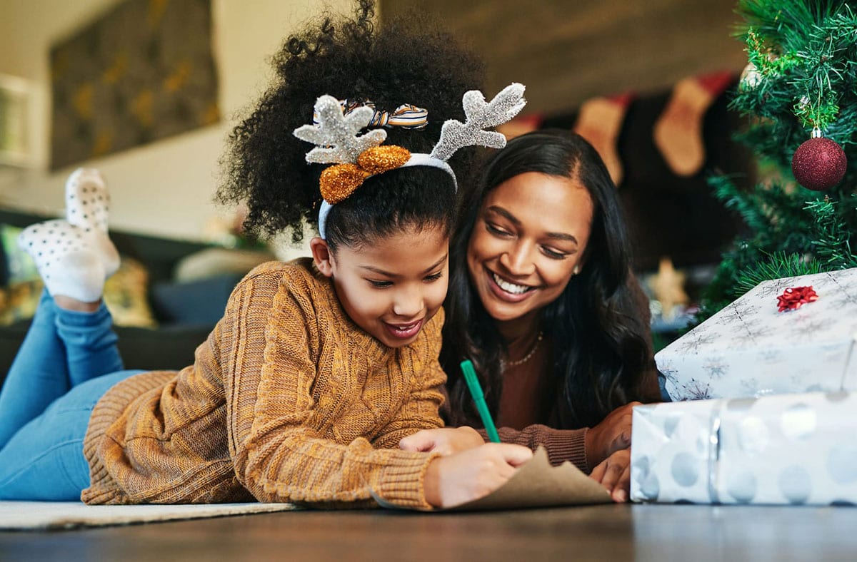 girl and mom writing in front of Christmas tree